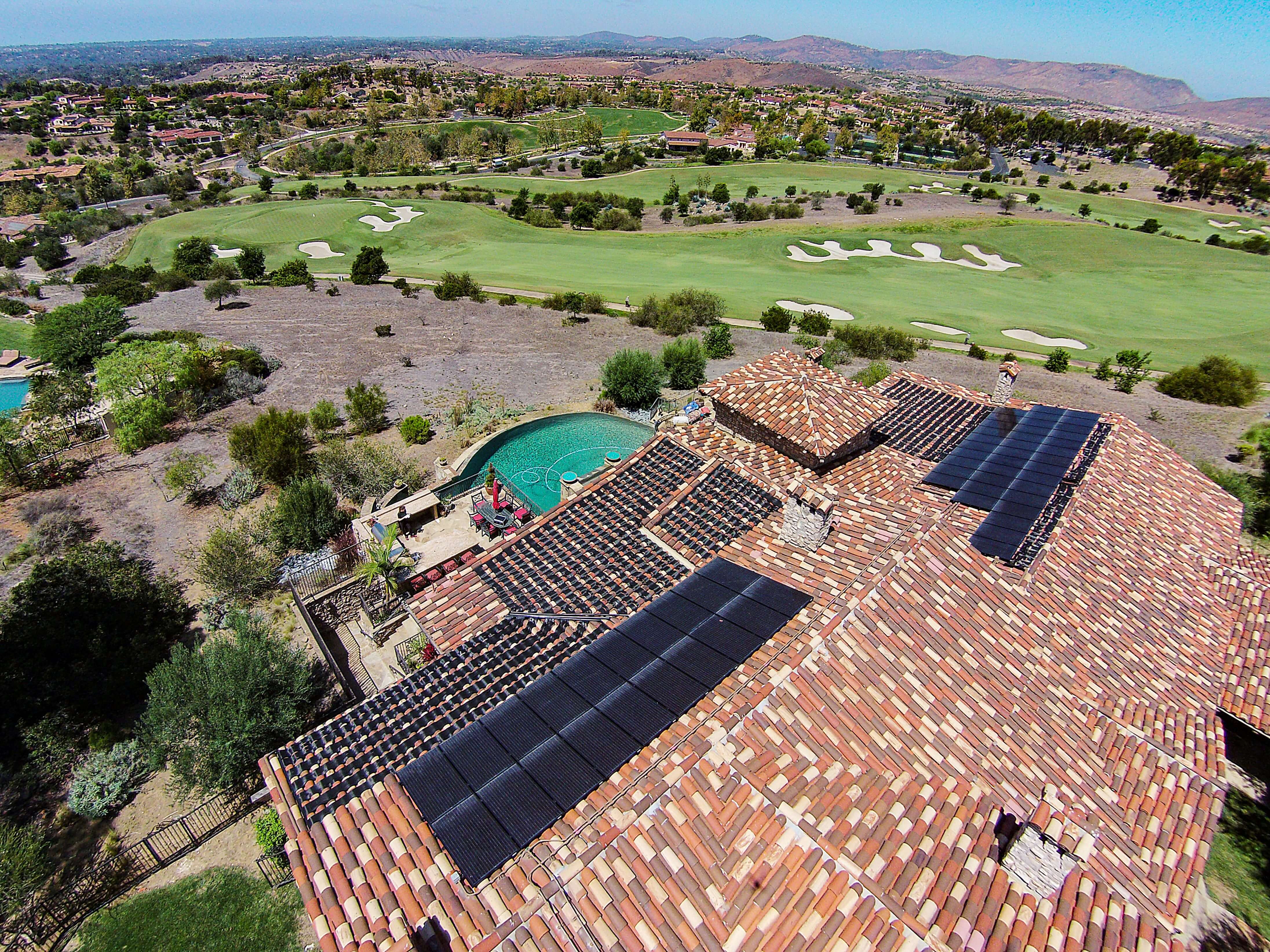 Aerial view of a large house with a terracotta tiled roof featuring solar panels emphasizing the house’s sustainable energy practices and its beautiful surroundings.