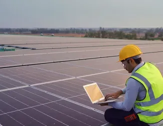 solar installer on roof looking over designs on computer