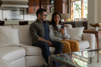 A couple sitting in their home, looking at a phone screen and discussing something together.
