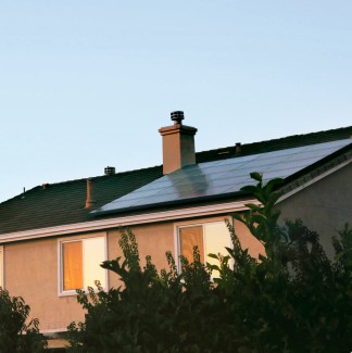 A residential house at dusk with a solar panel array installed on the roof.