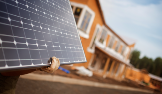 Person holding solar panel in front of house, ready for installation.