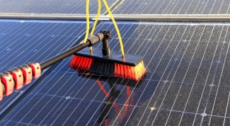 A broom is used to clear dust from solar panels, emphasizing the significance of regular cleaning for energy efficiency.