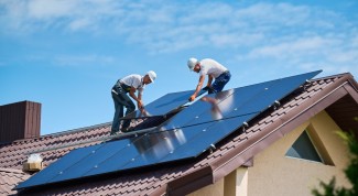 Two technicians collaborating on the installation of solar panels atop a building, promoting sustainable energy practices.