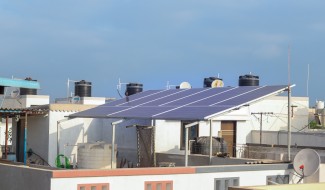 Residential rooftop with solar panels and water tanks on a sunny day in India, showcasing solar adoption in urban homes.