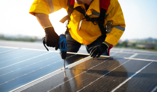 Technician in safety gear using a power drill to install or maintain solar panels on a commercial rooftop