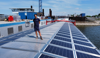 Wattlab team member standing on a cargo vessel outfitted with modular solar panels, docked at a maritime port in the Netherlands.