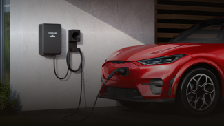 Red electric car charging at home with a wall-mounted EV charger