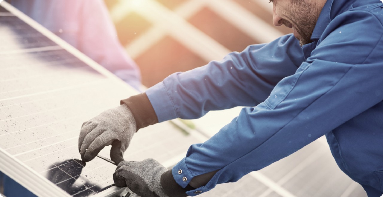 A man in a blue jacket and gloves carefully working on a solar panel outdoors.