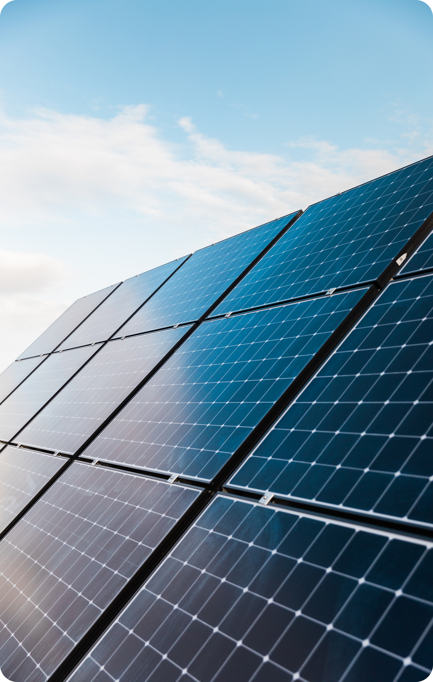 Array of blue monocrystalline solar panels angled toward a partly cloudy sky.